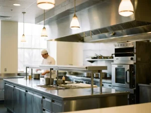 Professionele roestvrijstalen ziekenhuiskeuken met gepolijste werkbladen, industriële apparatuur en een kok op de achtergrond.